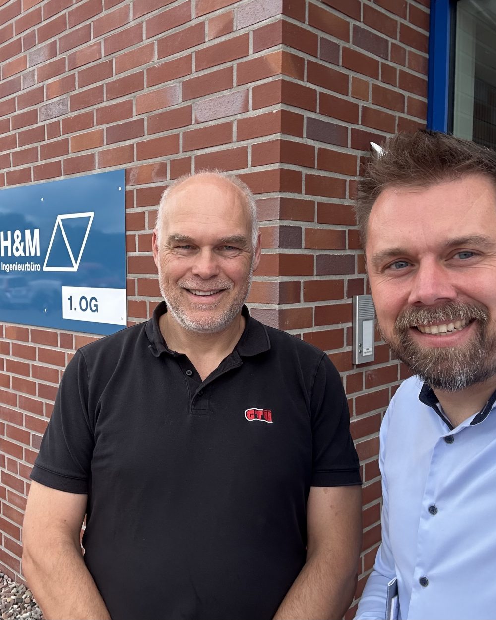 Thomas Bohlen und Joachim Duin vor dem Schild des H&M Ingenieurbüros in Hesel bei einem Unternehmensbesuch